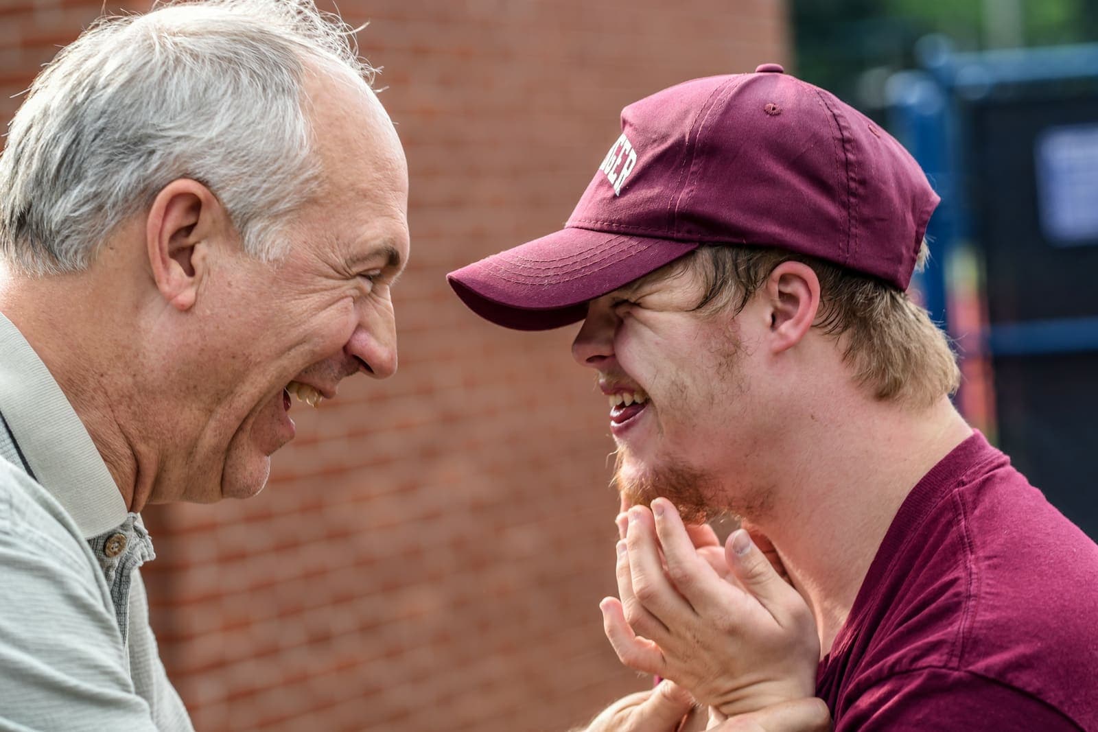 A young man with Down syndrome shares a laugh with an older man outdoors.